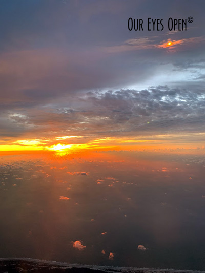 Rays of the sun reflect through the clouds high in the sky while on a jet plane.