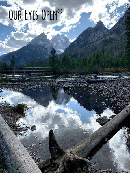 Cloud over in front of blue skies shading the sun giving us a perfect reflection with low water levels at the edge of String Lake in Grand Teton National Park.