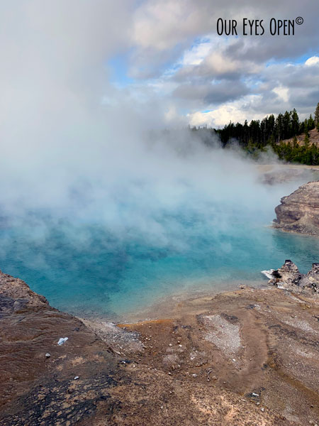 Turquoise water with a cloud of steam coming off one of the geysers in Yellowstone National Park.