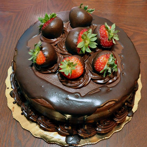 Round chocolate cake with chocolate covered strawberries on top.