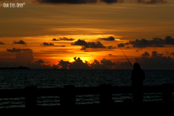 Someone fishing off the Skyway Bridge fishing pier in St. Petersburg, Florida with a beautiful orange, brown and gray sky sunset in the background.